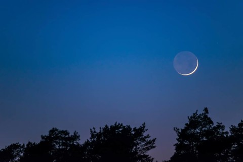 Very narrow, fine crescent moon with visible moon disc stands one day after the new moon over a