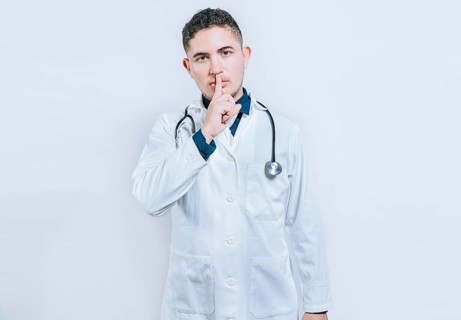 Doctor making silence gesture on white background. Latin doctor silencing and looking at the camera
