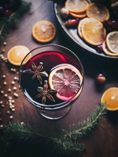 Glass of traditional mulled wine with orange and cranberry garnishes on a cozy Christmas table. The