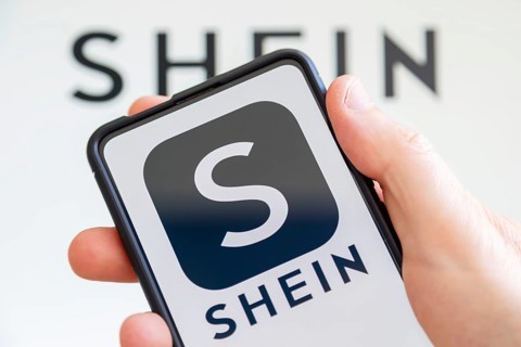 Hand holding mobile phone with Shein logo online marketplace online trading ecommerce computer