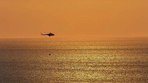 Helicopter, helicopter, fire-fighting helicopter, close over the sea, sunset, sun reflections on