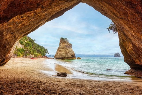 View from a cave onto a beach and isolated rocks in the sea, under a cloudy sky, Cathedral Grove,