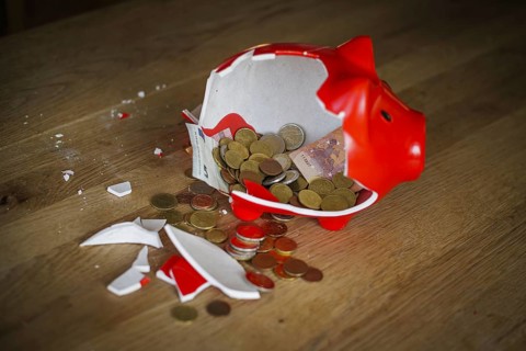 Symbolic photo on the subject of saving. An open, broken piggy bank with coins and banknotes stands