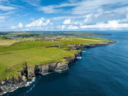 Aerial view of rugged cliffs on the North Sea coast, with the harbour town of Wick on the horizon,