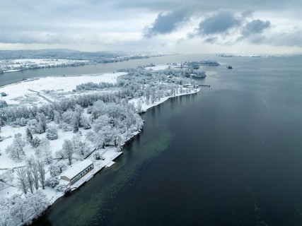 Aerial view of the snow-covered Mettnau peninsula with the Mettnaupark, on the horizon the island