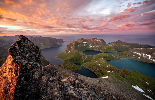View over mountain top and sea, dramatic sunset, at the summit Hermannsdalstinden, with lakes