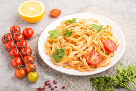 Semolina pasta with tomato pesto sauce, orange and herbs on a white ceramic plate on a gray