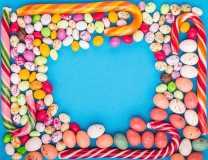 Colorful frame of multicolored candies on a blue background. Christmas cane, chocolate eggs,