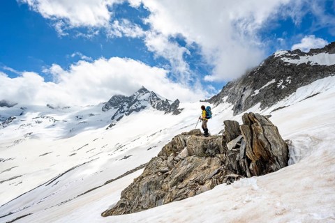 Mountaineer on a rock between snow, descent from the summit of Schönbichler Horn, view of