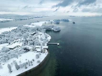 Aerial view of the snow-covered Mettnau peninsula with the Mettnau park, spa centre and beach café,