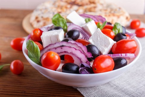 Greek salad with fresh cherry tomatoes, feta cheese, black olives, basil and onion on wooden