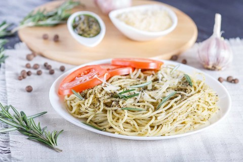 Spaghetti pasta with pesto sauce, tomatoes and cheese on a linen tablecloth. close up, selective