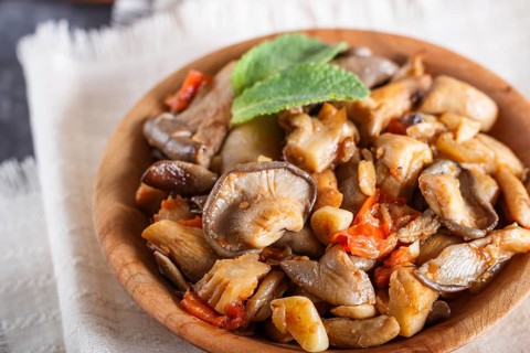 Fried oyster mushrooms with tomatoes in wooden plate on black concrete background. top view, close