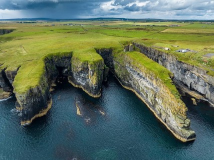 Aerial view of the ruined Castle of Old Wick surrounded by rugged cliffs on the North Sea coast,