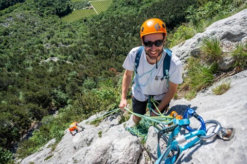 A smiling climber in a safety helmet secures himself to a rock with ropes and carabiners, Alpine