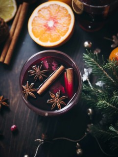 Glass of traditional mulled wine with orange and cranberry garnishes on a cozy Christmas table. The