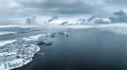Aerial panorama of the snow-covered Mettnau peninsula with the Mettnau park, spa centre and beach