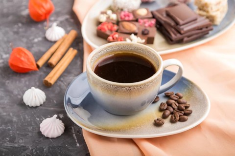 A cup of coffee with chocolate and coconut candies on a black concrete background and orange