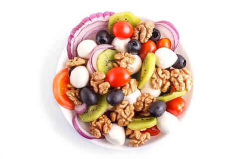 Salad with cherry tomatoes, mozzarella cheese, black olives, kiwi, and walnuts isolated on white