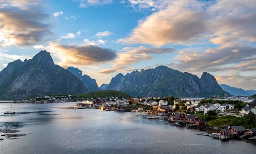 Village view of the fishing village Reine, traditional red Rorbuer cabins, at sunset, in the back