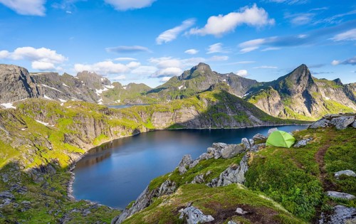 Green camping tent, mountain landscape with lake Tennesvatnet, at sunrise, behind peak of