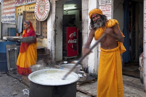 Hindu man wearing red bindi on forehead stirring food in huge pot for the needy in Udaipur,