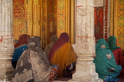 Muslim women wearing colourful headscarfs and saris praying at the Nizam-Ud-Din shrine in Delhi,