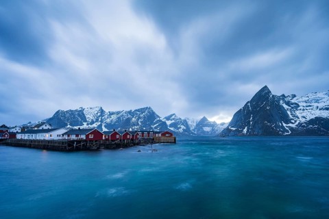 Rorbuer cabins of Hamnoy by the fjord, snowy mountains in the back, Hamnoy, Reine, Moskenesoya,