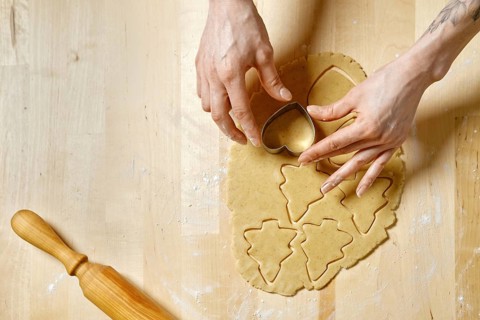 Top view at hands of unrecognizable woman cutting out biscuits from dough with cookie cutter