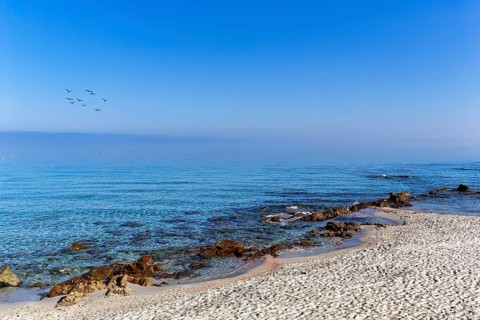 Coastline in the morning mist, sandy beach with rocks by the sea, blue sky, L'Île-Rousse, Ile