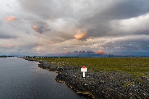 Small lighthouse at the coast, behind the mountain range Seven Sisters, light mood with rainbow,