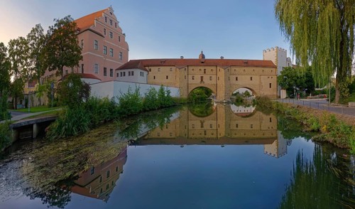 An old fortification wall town spectacle is perfectly reflected in the calm waters of the river