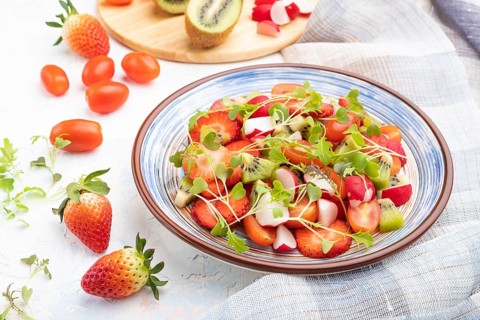 Vegetarian fruits and vegetables salad of strawberry, kiwi, tomatoes, microgreen sprouts on white