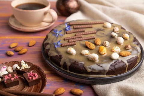 Homemade chocolate brownie cake with caramel cream and almonds with cup of coffee on a colored