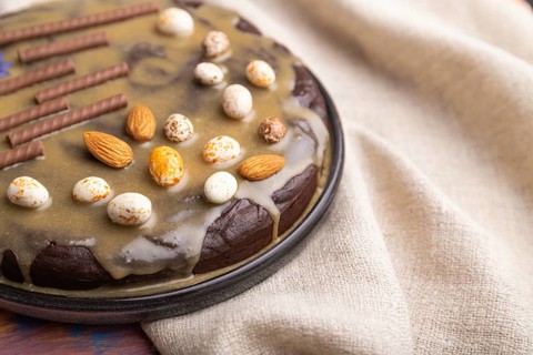 Homemade chocolate brownie cake with caramel cream and almonds with cup of coffee on a colored