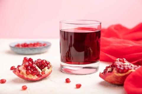 Glass of pomegranate juice on a white and pink background with red textile. Side view, close up,