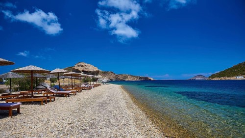 An empty beach with deckchairs and straw umbrellas on the clear blue waters of a sea under a bright