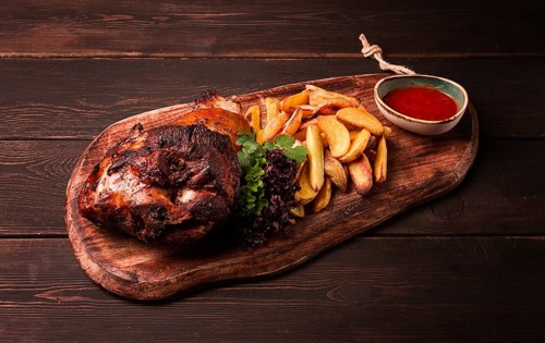 Pork knuckle, in soy-honey sauce, with fried potatoes, on a wooden chopping board, homemade, no