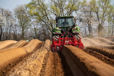 A farmer builds asparagus ridges on a field with the help of an asparagus tiller, in which the