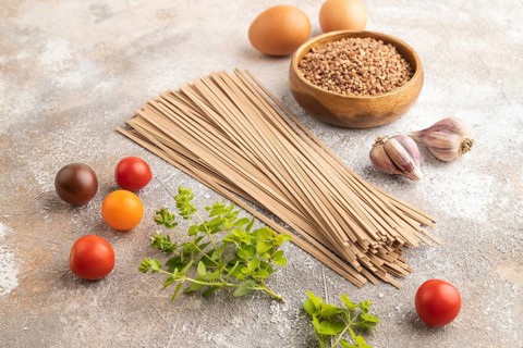 Japanese buckwheat soba noodles with tomato, eggs, spices, herbs on brown concrete background. Side
