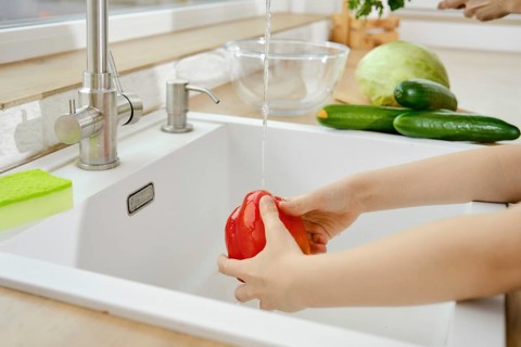 Closeup view of hands of kid washing bell pepper in the sink