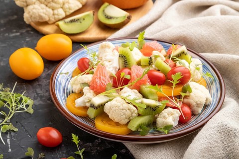 Vegetarian salad of cauliflower cabbage, kiwi, tomatoes, microgreen sprouts on black concrete