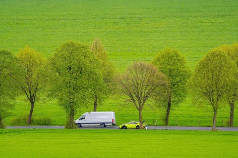 Car on a country road, overtaking manoeuvre, green fields, meadows, trees line the 2-lane road,