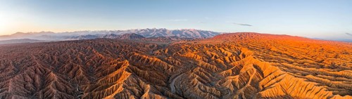 Panorama, riverbed runs through a landscape of eroded hills, badlands at sunrise, mountain peaks of