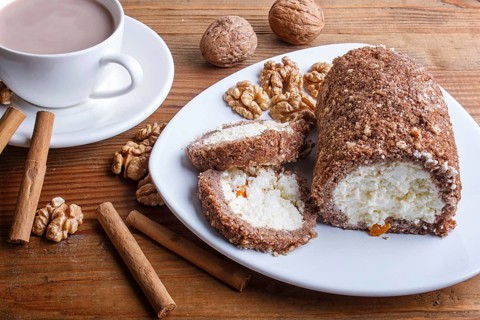 Roll cake with curd and walnuts isolated on brown wooden background, close up