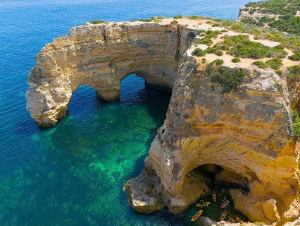 Large rock formations with natural arches on the coast, near water with canoes, aerial view, Praia