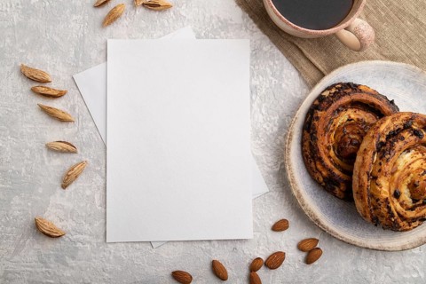 White paper invitation card, mockup with almonds, bun, cup of coffee, linen textile on gray