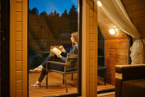 View through the window of a young woman sitting on the terrace in the evening with a book
