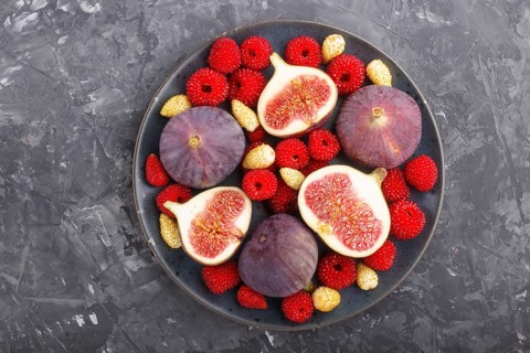 Fresh figs, strawberries and raspberries on blue ceramic plate on black concrete background. top