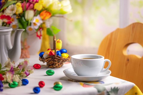 A coffee cup on a table with Easter decorations and a colourful bouquet of spring flowers in the